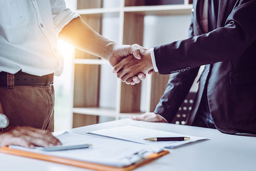 About Our Agency - Closeup View of Businessman and Insurance Agent Meeting in an Office with Paperwork on the Table Shaking Hands