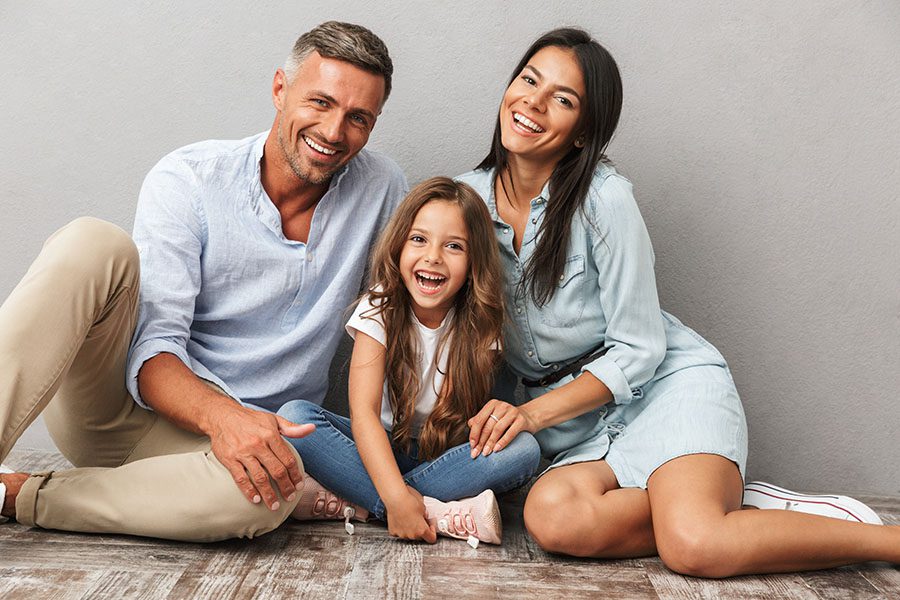 Personal Insurance - Portrait of Happy Family with Young Daughter Sitting on the Floor in Their Home